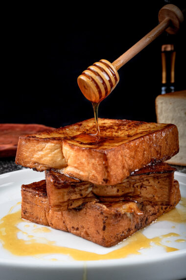 Golden French toast stack with pat of butter and honey drizzle on white plate