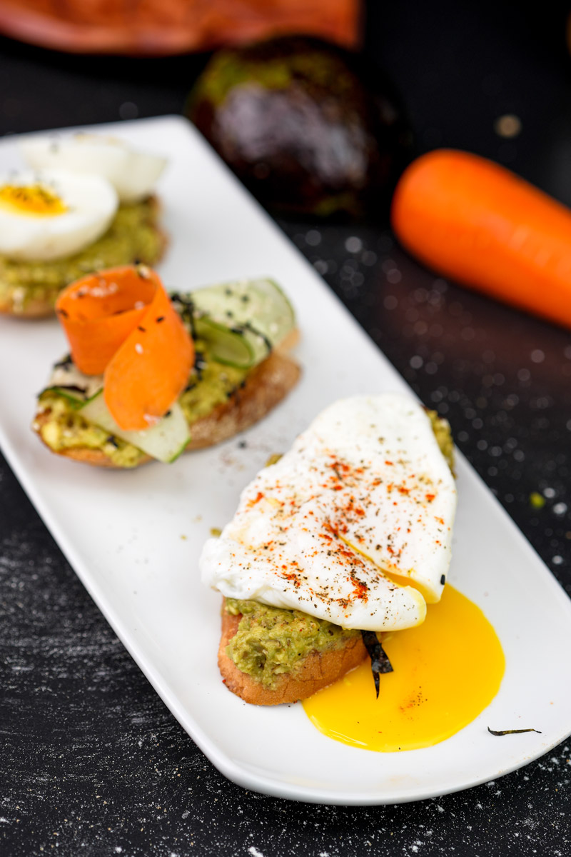 Gourmet avocado toast trio with poached egg, cucumber and carrot garnish
