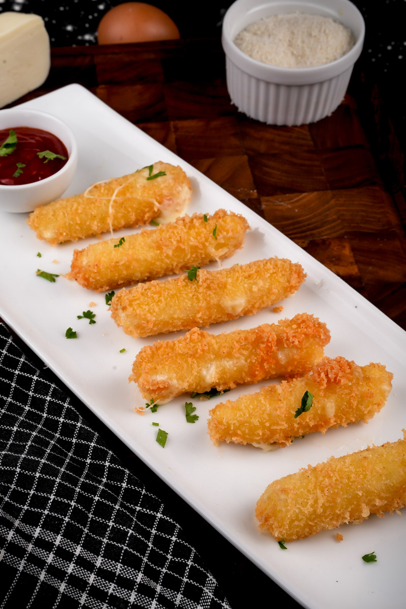 Homemade mozzarella sticks arranged on white serving plate with marinara dipping sauce