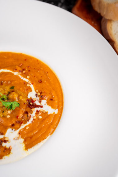 Close-up of spiced lentil tomato soup with cream and fresh herbs