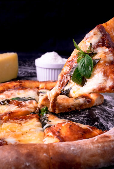 Slice of Margherita pizza being pulled with stretchy mozzarella