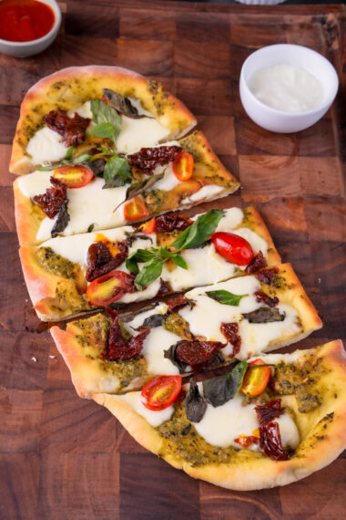 Homemade pesto pizza with sun-dried tomatoes and stretchy cheese