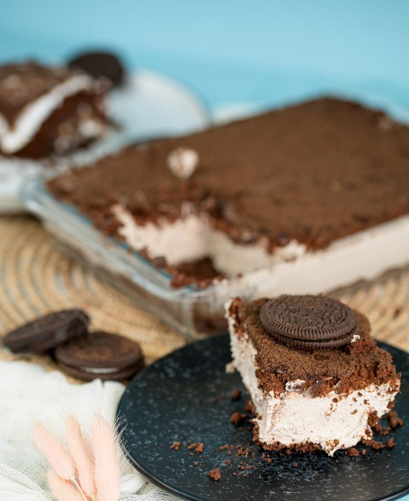 Oreo dirt cake slice on black plate with chocolate sandwich cookies