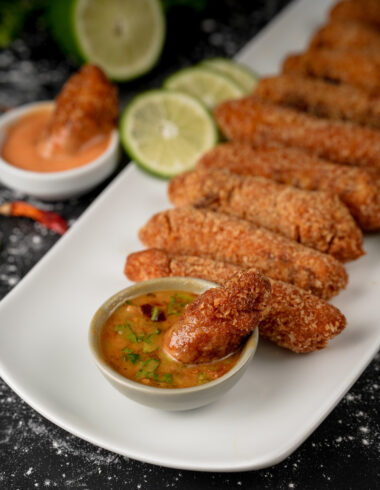 Close-up of peri peri fish strips served with lime slices and spicy sauce