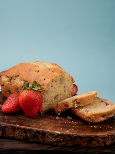 Strawberry pound cake on wooden board with fresh strawberries against blue background