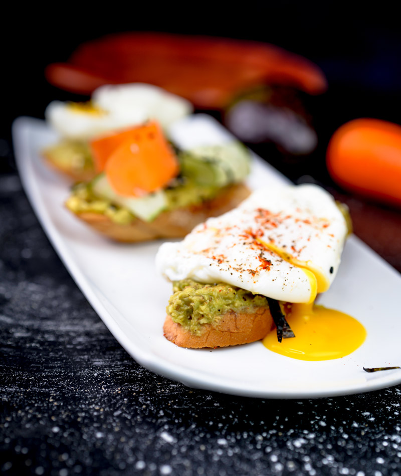 Three varieties of avocado toast with egg, cucumber and carrot on serving plate