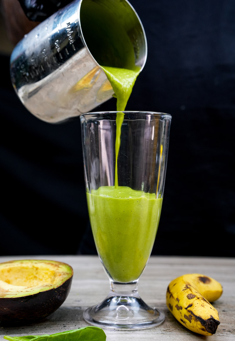 Pouring green avocado spinach smoothie into glass