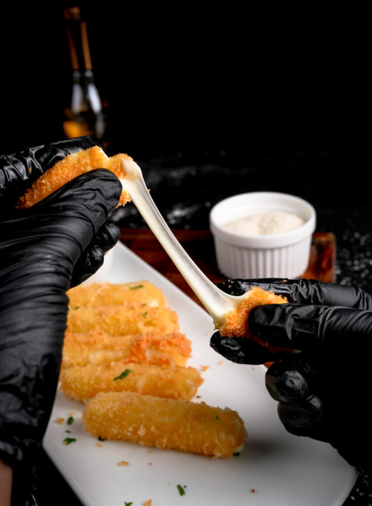 Cheese sticks being pulled apart showing stretchy mozzarella with marinara dipping sauce