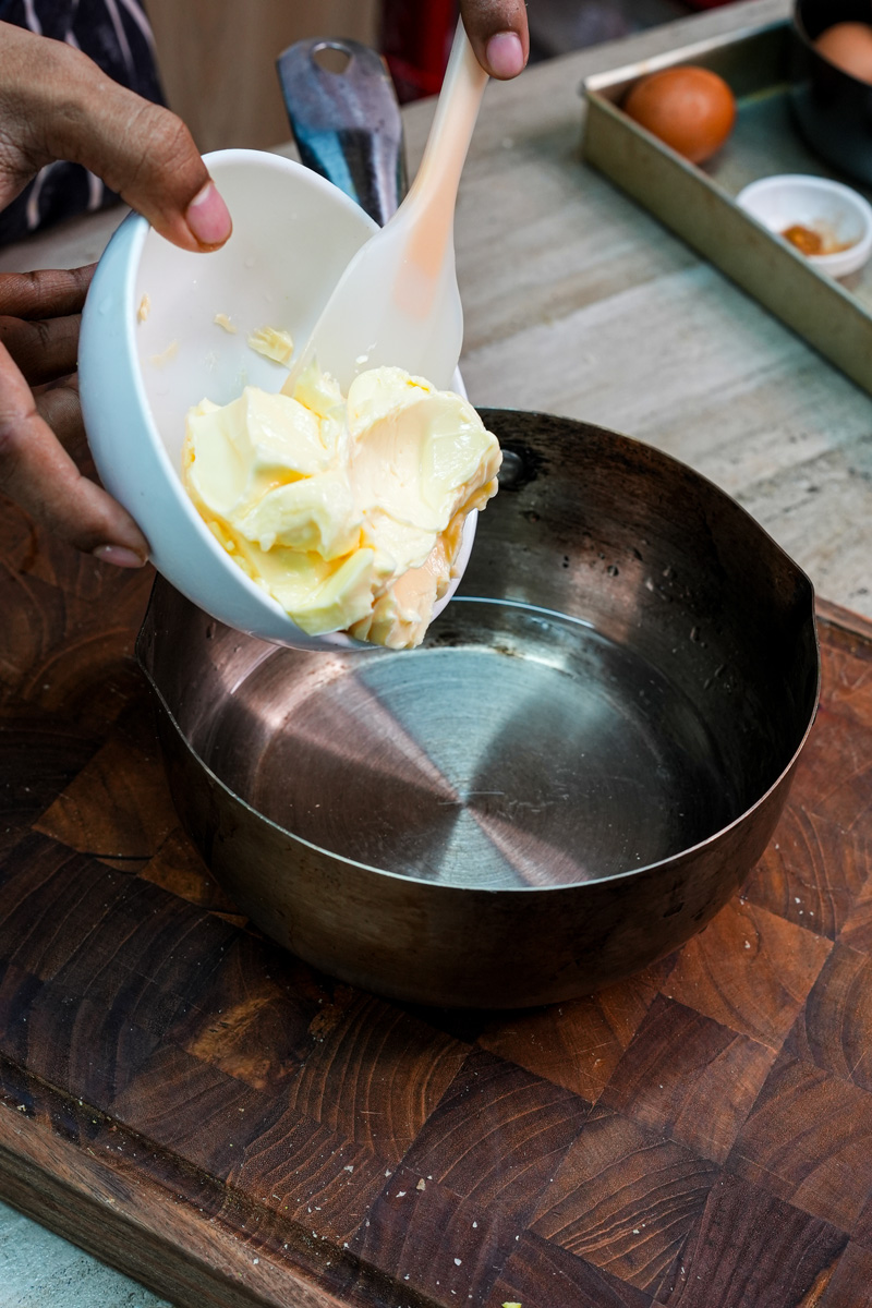 Adding butter to saucepan for choux pastry dough preparation