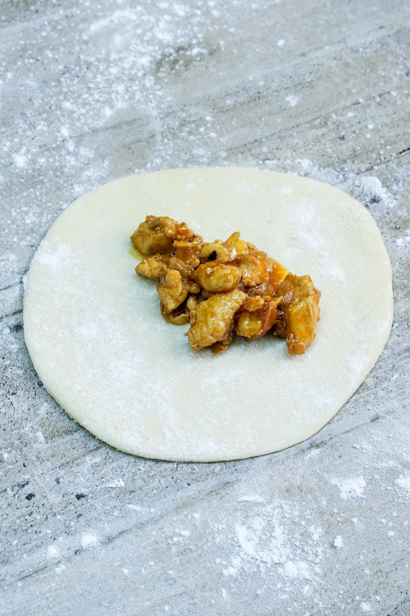 Adding chicken filling to empanada dough circle