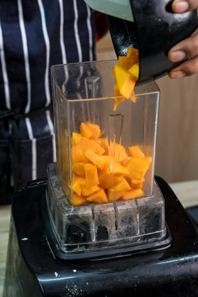 Adding diced mango chunks to blender for mango muffin recipe