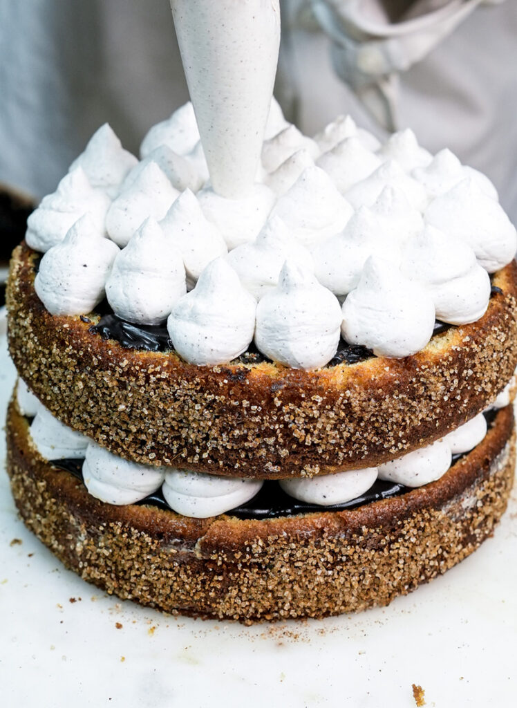 Adding final cream layer to churro cake assembly with piping bag