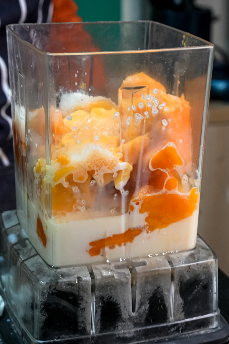 Adding milk to mango pieces in blender during preparation