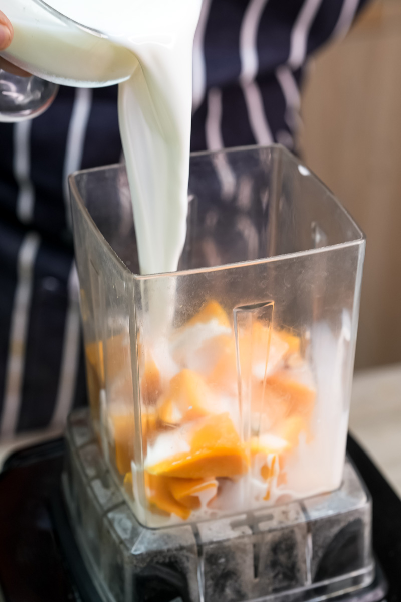 Adding milk to mango pieces in blender