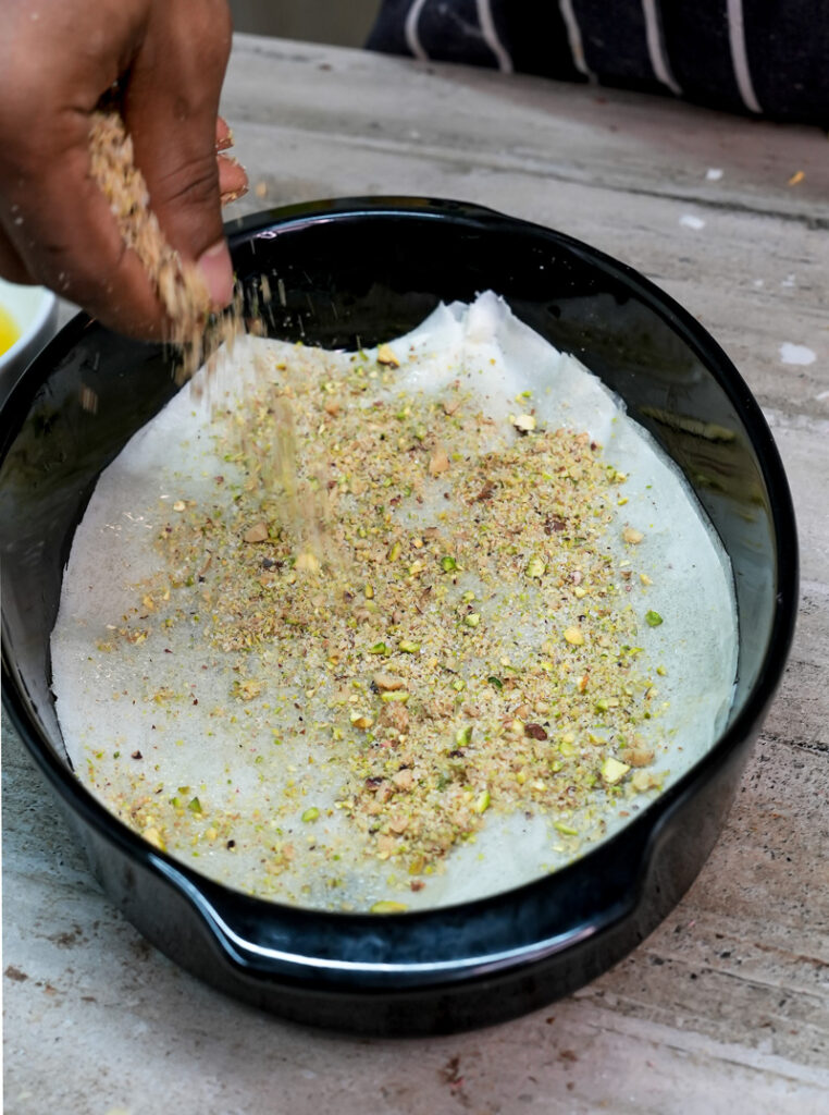 Adding pistachio filling to baklava layers