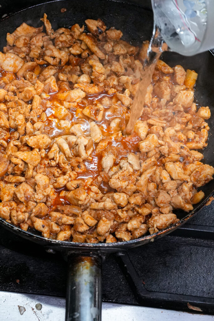 Adding sauce to chicken empanada filling