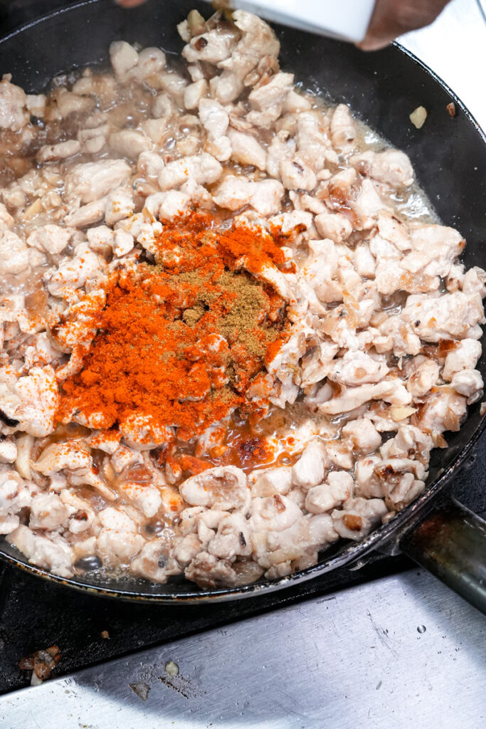 Adding spices to chicken empanada filling
