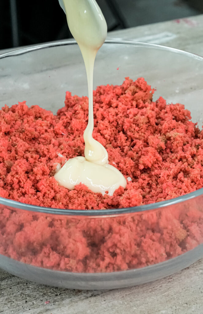Adding white frosting to red cake crumbs for strawberry cake pop mixture