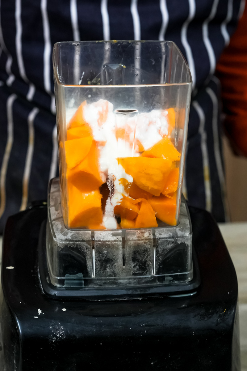 Adding yogurt to mango pieces in blender jar