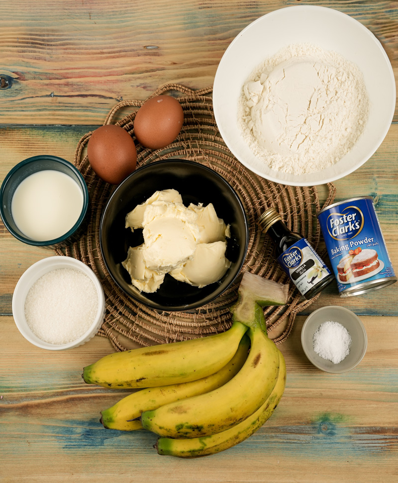 Banana pound cake ingredients including ripe bananas, flour, eggs, butter, and baking essentials on wooden surface