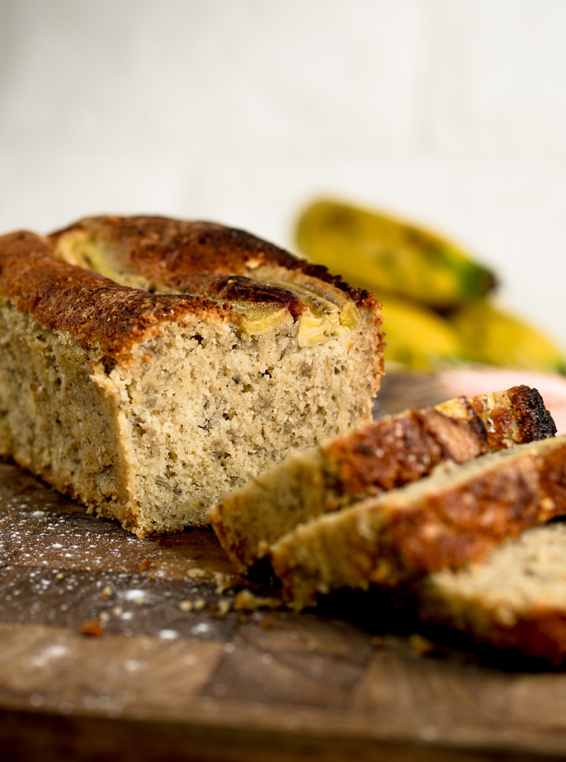 Sliced banana pound cake with golden brown crust and moist crumb on wooden cutting board