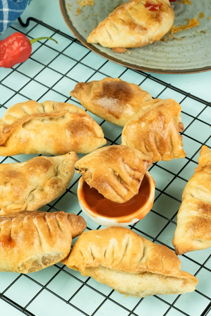 Batch of chicken empanadas on cooling rack with sauce