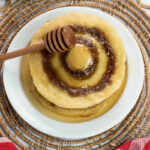 Breakfast cinnamon roll pancakes with honey dipper on wicker placemat