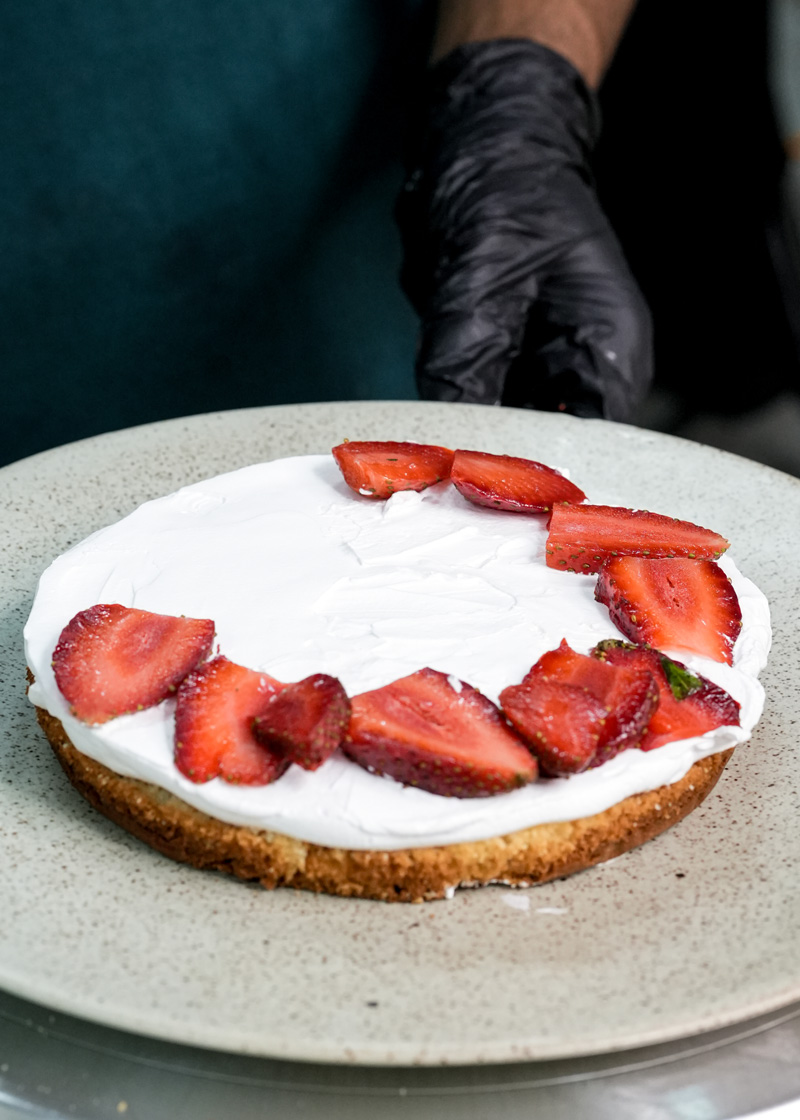 Cake layer with strawberries arranged in circle on whipped cream base