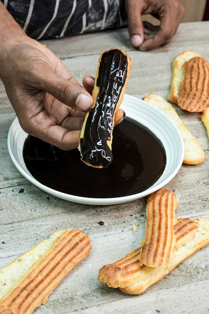 Chocolate-glazed eclair being lifted from melted chocolate coating bowl