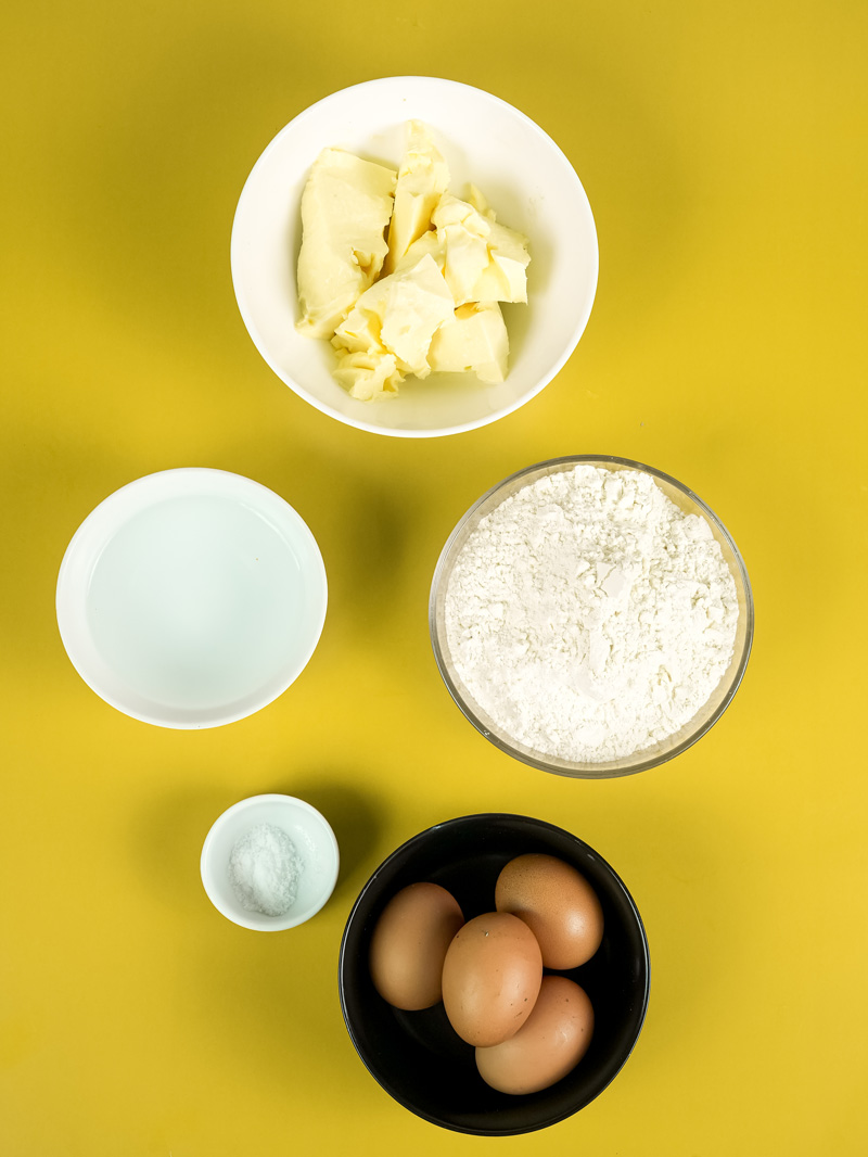 Choux pastry ingredients: butter, flour, eggs, milk and salt in bowls
