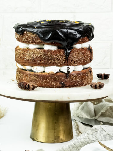 Churro cake with chocolate ganache drip and cinnamon sugar layers on gold cake stand