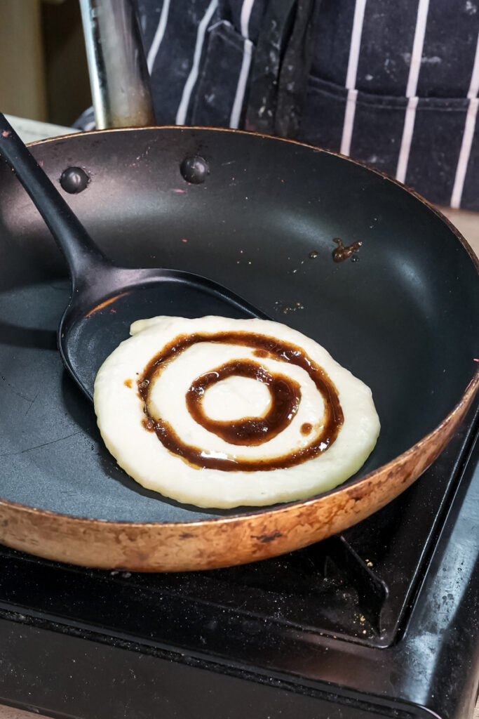 Cinnamon roll pancake cooking in cast iron pan with spiral swirl pattern