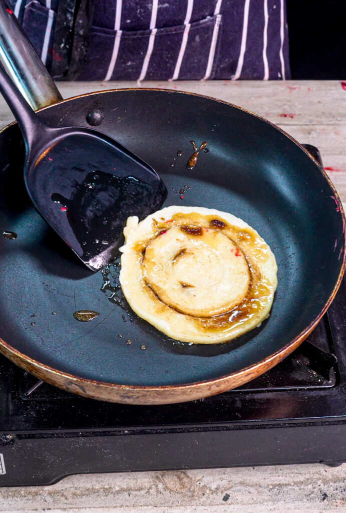 Cinnamon roll pancake with swirl pattern cooking in cast iron skillet
