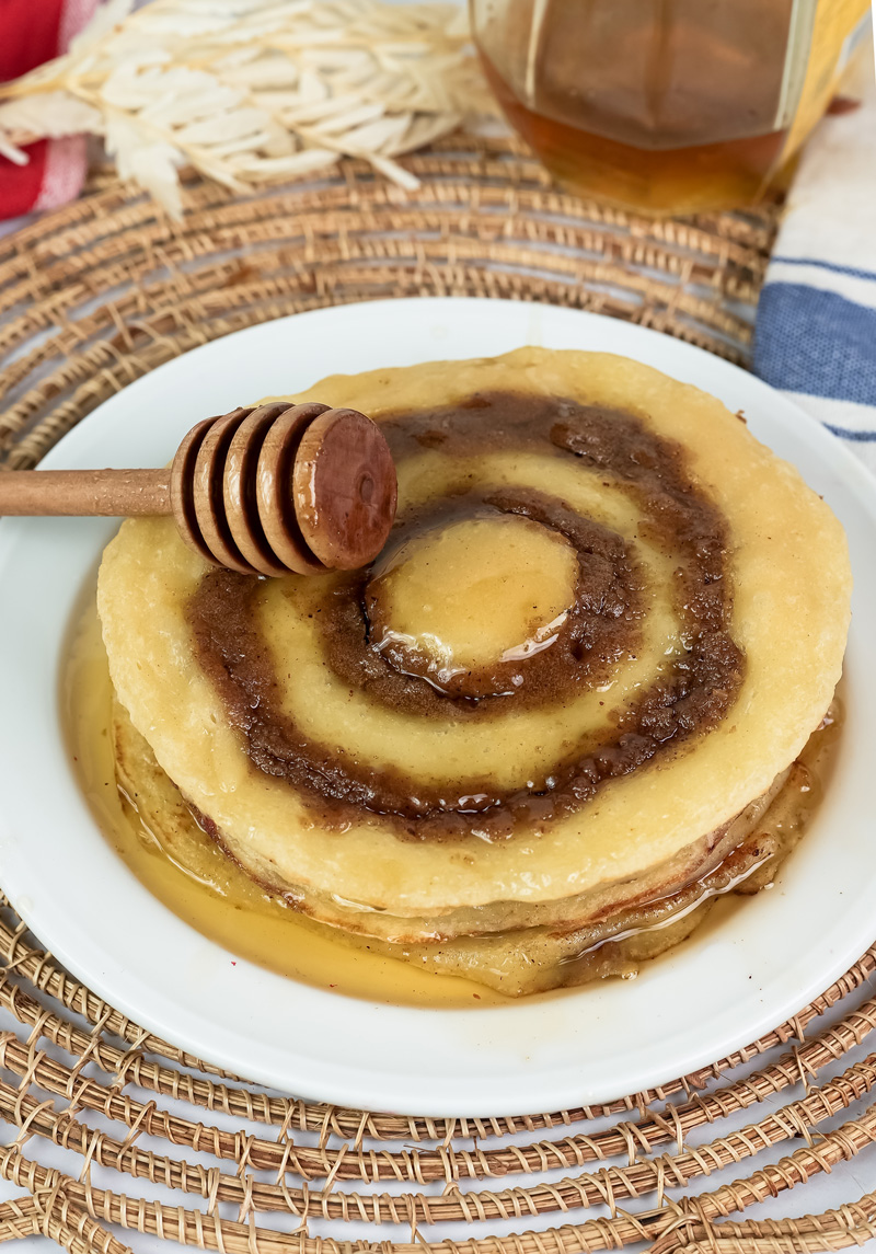 Cinnamon roll pancakes topped with honey and wooden honey dipper