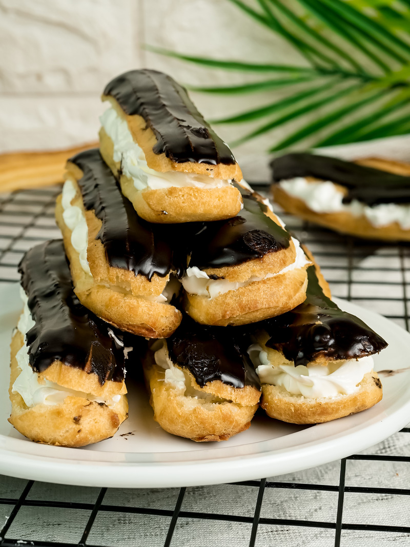 Classic French eclairs with vanilla cream filling and chocolate glaze stacked on white plate