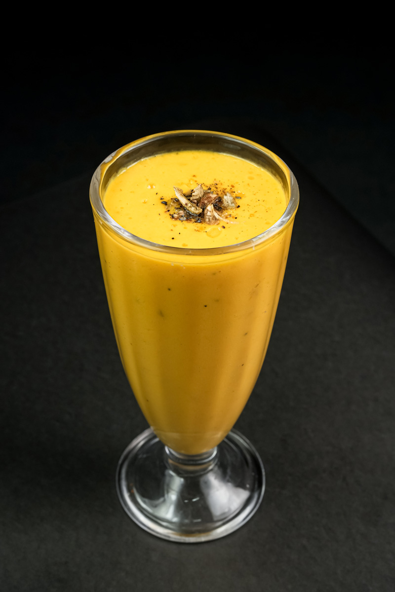 Creamy mango lassi in tall glass with spice topping