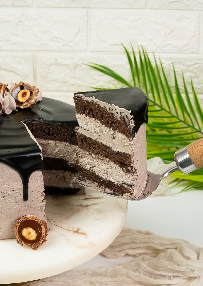 Serving slice of layered Ferrero Rocher cake with chocolate frosting