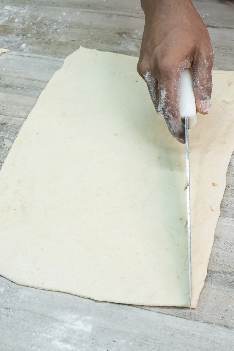 Cutting croissant dough into triangular strips with knife