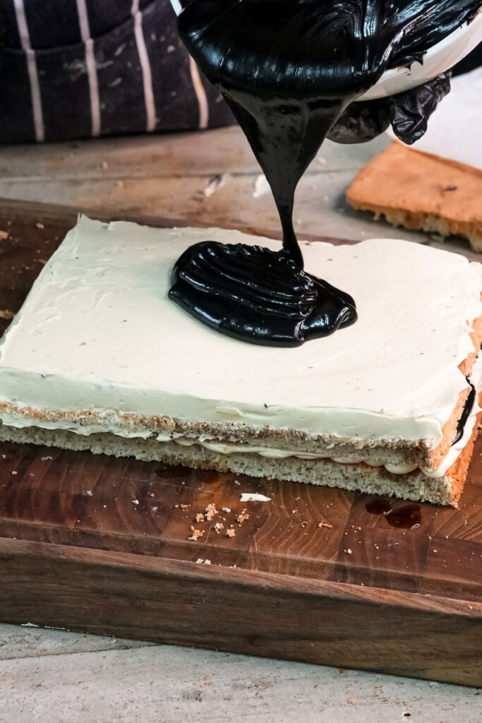 Dark chocolate glaze being poured onto opera cake final layer