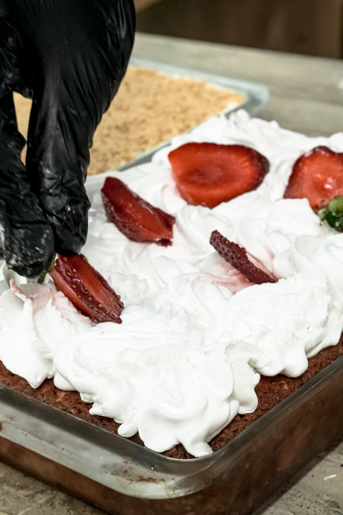 Decorating strawberry earthquake cake with whipped cream and fresh strawberries