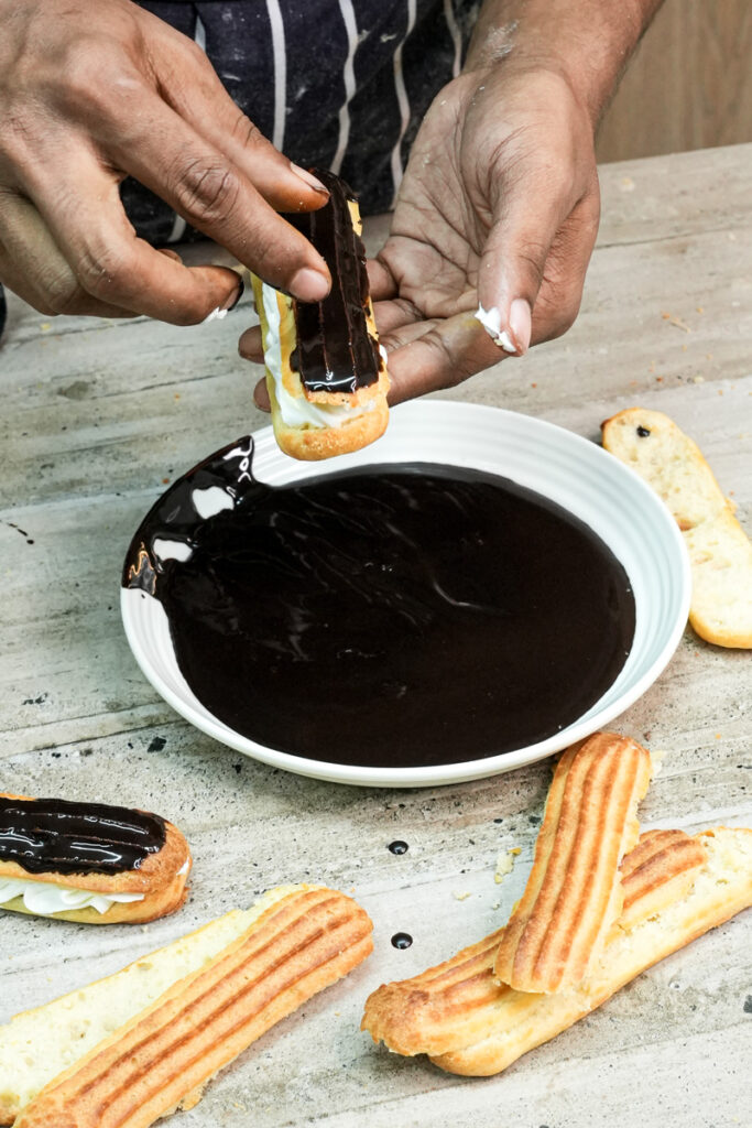 Dipping assembled cream-filled eclair into chocolate glaze for finishing touch