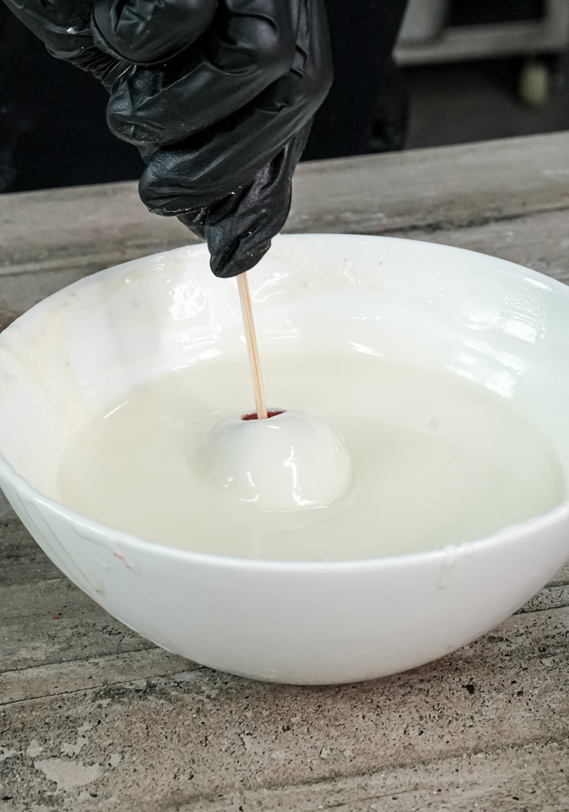 Dipping cake pop stick in melted white chocolate coating
