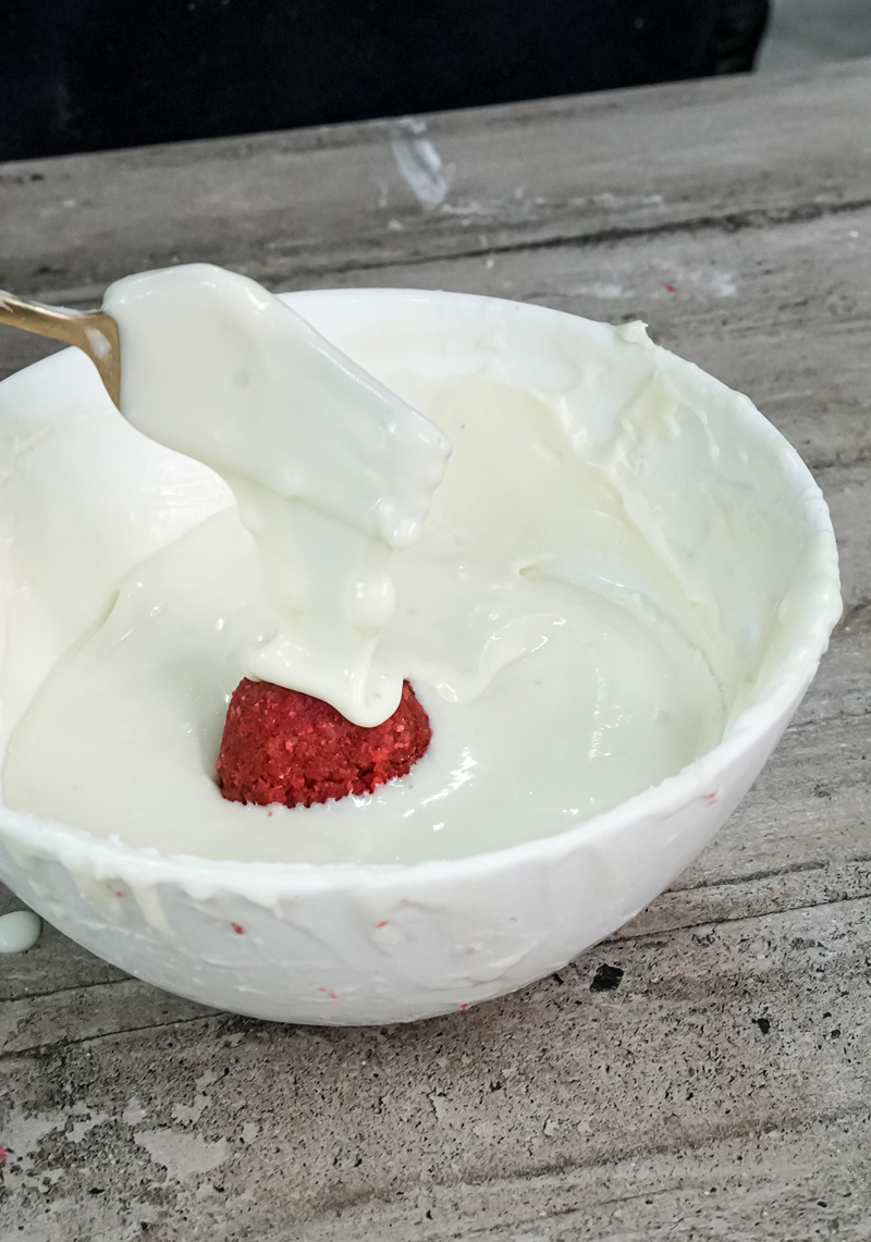 Dipping strawberry cake ball in white chocolate for coating