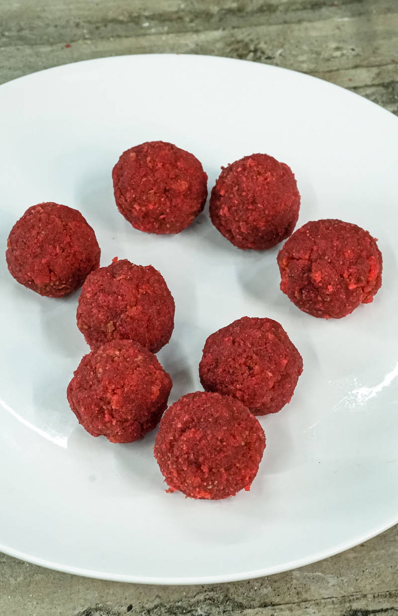 Eight strawberry cake balls arranged on white plate before coating