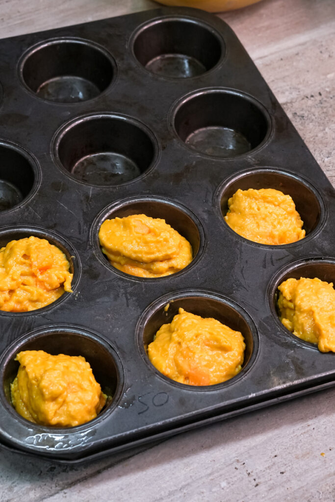 Filling muffin cups with golden mango batter