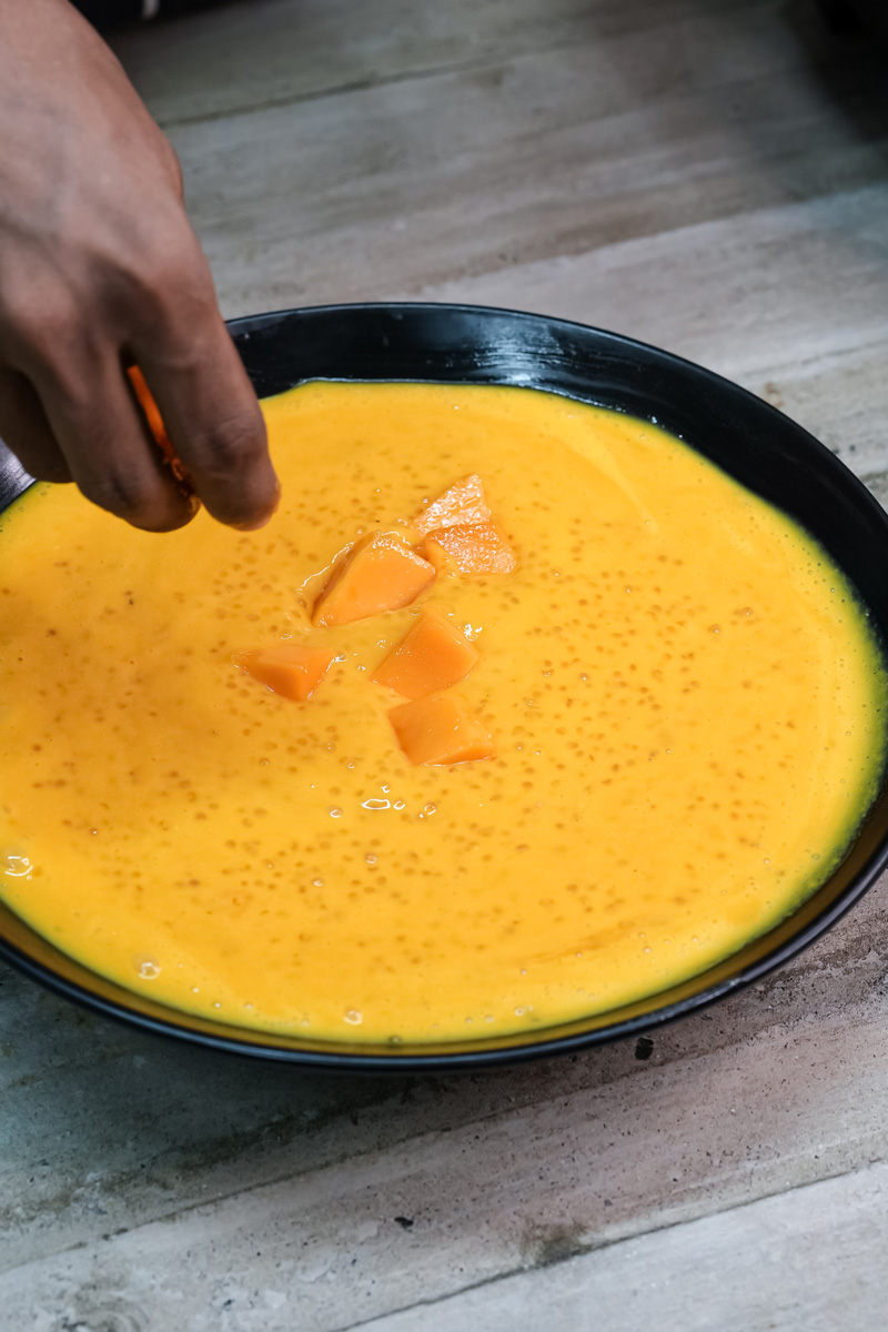 Finished mango sago dessert with mango pieces in black bowl