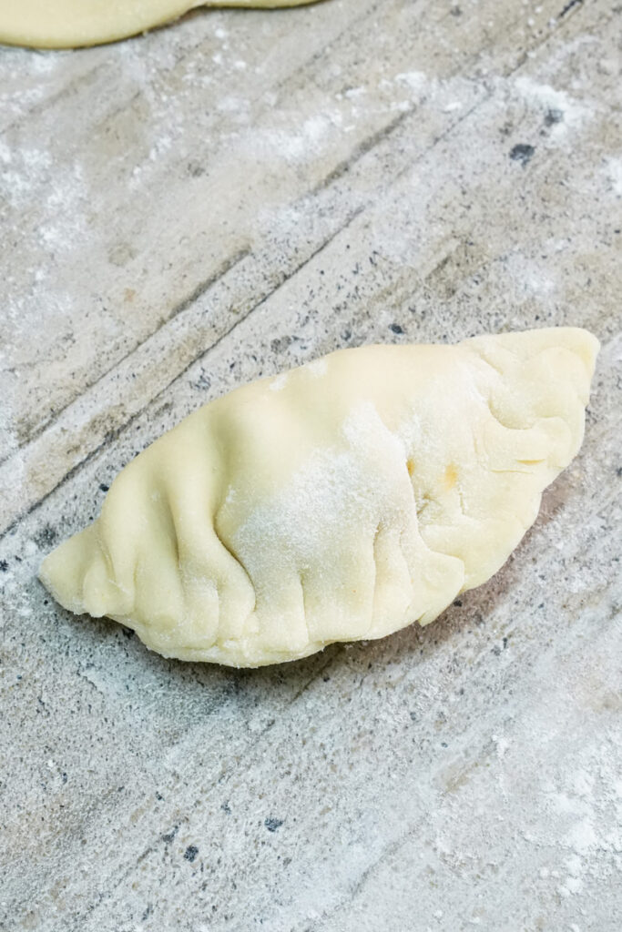 Folding empanada dough around chicken filling