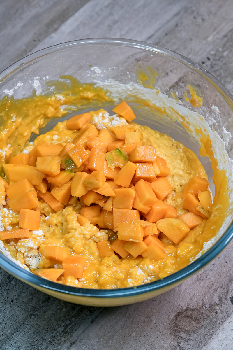 Folding fresh mango pieces into muffin batter