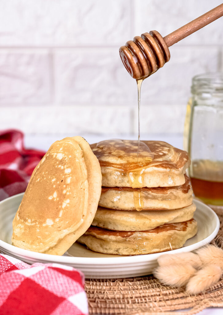 Fresh honey streaming onto homemade gluten free pancakes from wooden honey stick