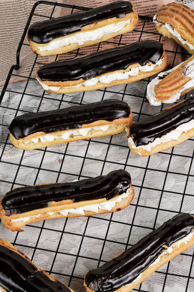 Freshly baked eclairs with chocolate glaze cooling on wire rack